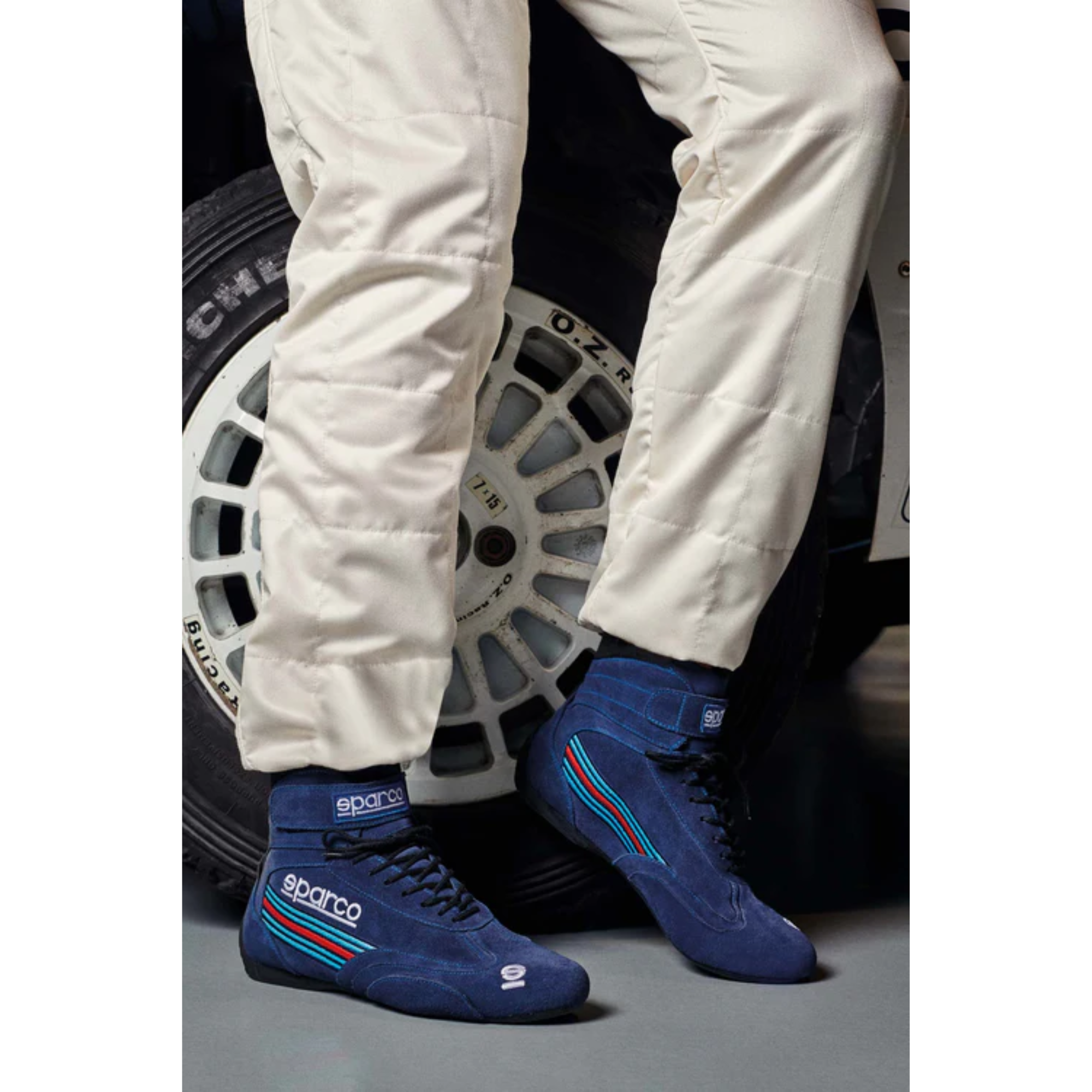 The navy Sparco Martini Top Racing Shoes worn by a driver in a garage beside a car.