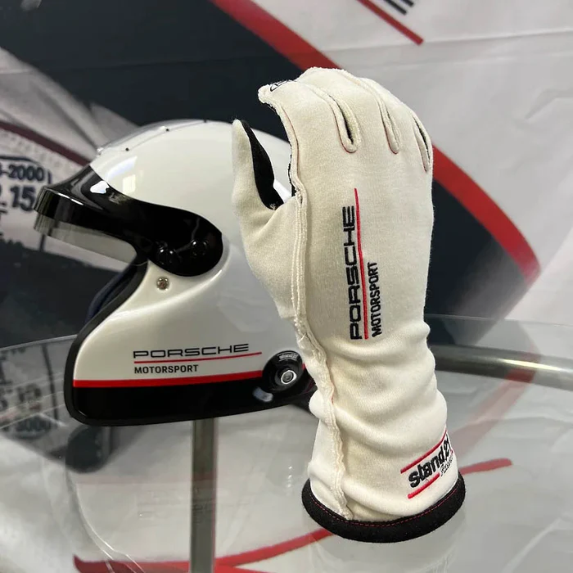The white Stand-21 Porsche Motorsports Legacy Racing Gloves from Stand 21 on display at a race.