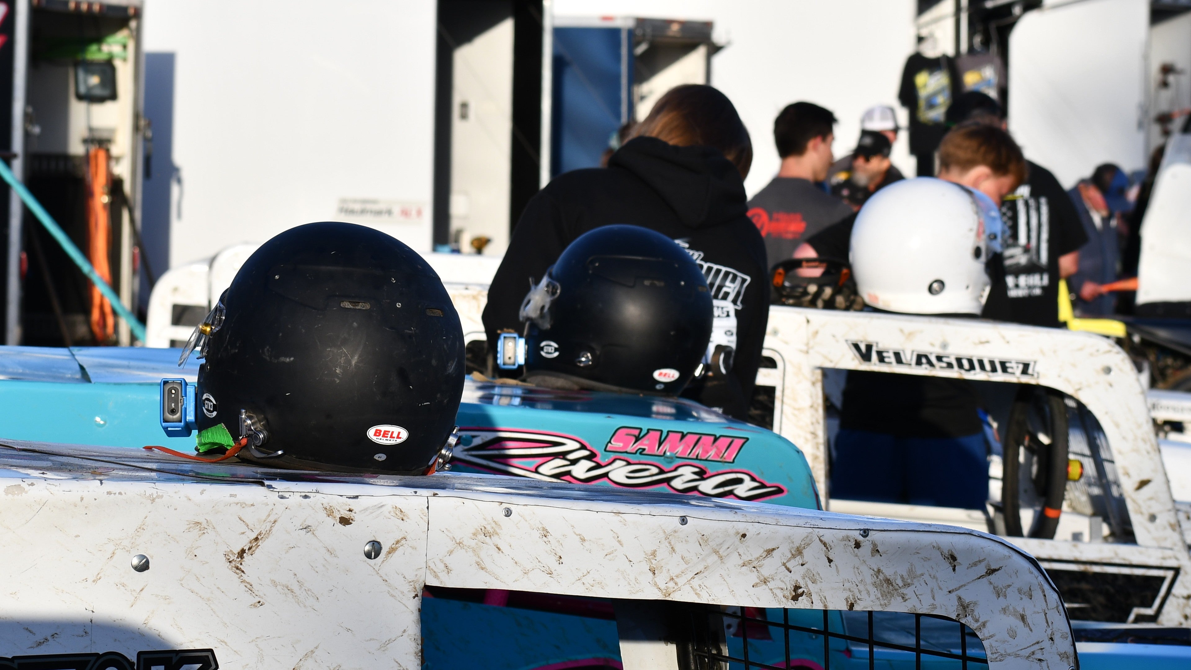 Three dirt racing cars with Bell auto racing helmets on top at the Watsonville Speedway, featuring drivers Sammi Rivera and Mr. Velasquez.