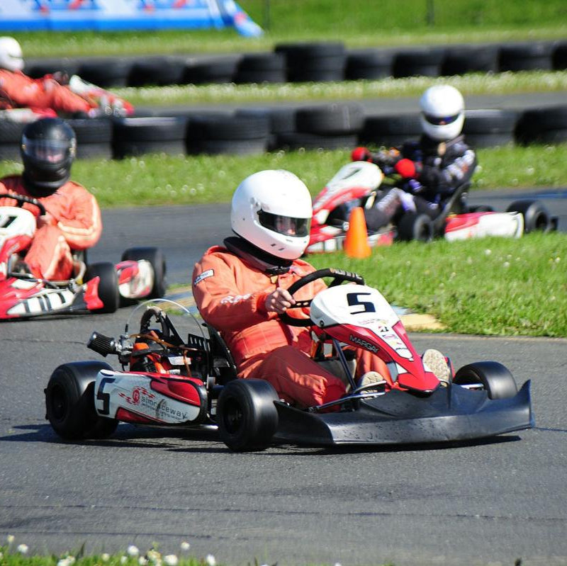 People racing go-karts on a track with grass and tires in the background at Sonoma Raceway.
