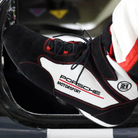 The black and white Stand-21 Porsche Motorsports Daytona3 Racing Shoes from Stand 21 in a driving lifestyle image.