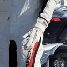 The white Stand-21 Porsche Motorsports Legacy Racing Gloves from Stand 21 worn by a driver in the paddock.